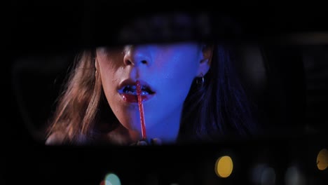 woman mirrored in rear view mirror apply red lipstick in car before date at night