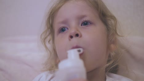 sad girl breathes with inhaler lying in bed near beige wall