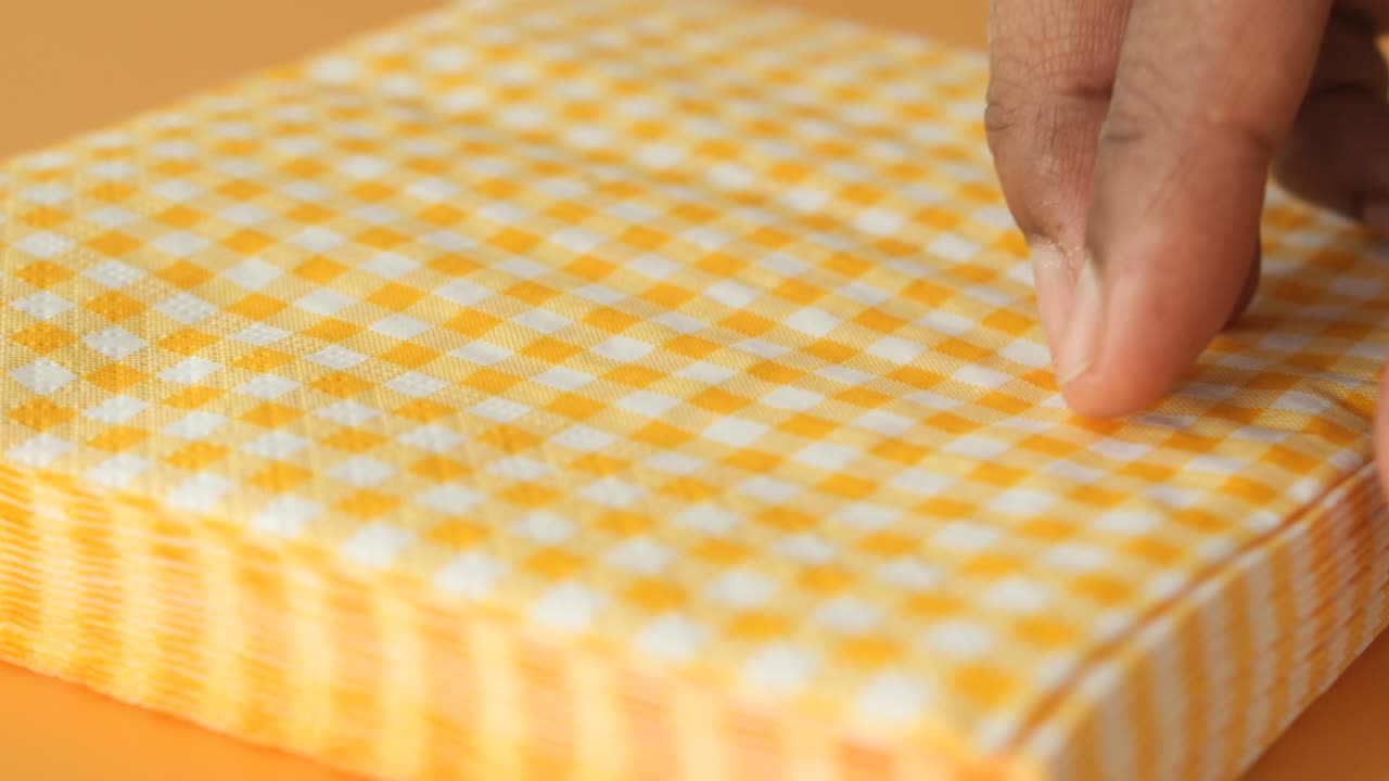 mano abriendo una pila de servilletes a cuadros amarillos