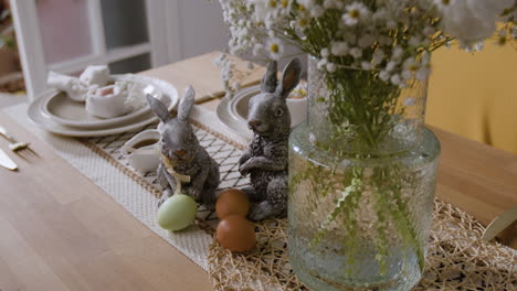 messa in tavola di pasqua con statuette di conigli e fiori