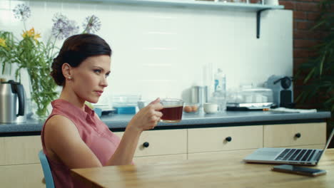 Businesswoman-watching-laptop-with-cup-of-tea-in-kitchen.-Girl-surfing-internet.