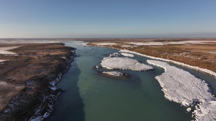 Aerial view of the Urriðafoss River in Iceland, featuring floating ice formations and contrasting winter landscapes under a clear blue sky.