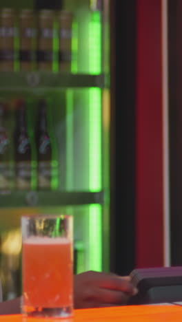 barman barbudo dá conta ao hóspede no balcão do bar. barman sorridente prepara cheque de pagamento para mulher em clube noturno. negro positivo trabalha em pub