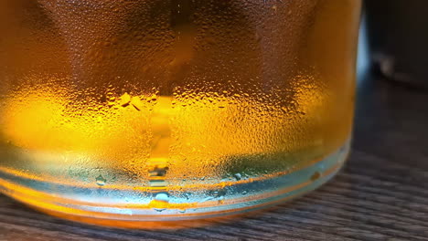 close-up of a cold beer glass with condensation on a wooden table in a cozy setting