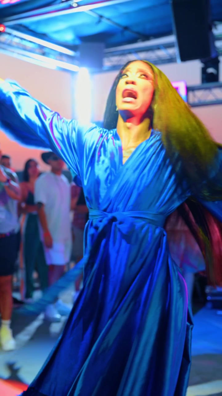 New York, USA, 28 Juni 2026: Penampil menari di samping layar LED di dek pesta kapal. Pemandangan dekat seseorang bergaun satin biru di bawah pencahayaan panggung magenta dan cyan.