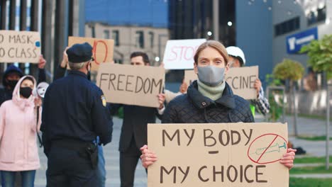 caucasian wearing facial mask holding my body my choice" signboard and looking at camera in a protest against covid 19"