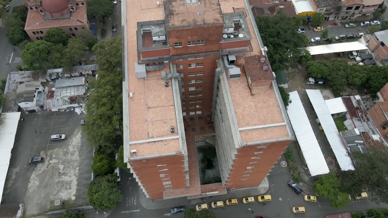Medellín’s sunset aerial, with warm hues over urban streets, mountains, and serene distant horizon, drone descends on building