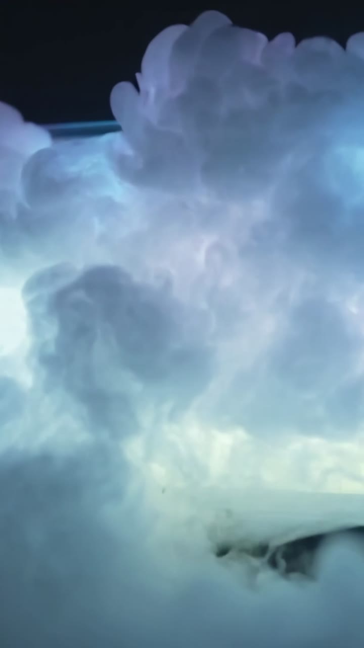 Vídeo vertical: Vapor azul espesso subindo, formando plumas ondulantes em estúdio, iluminado por monitor pastel.