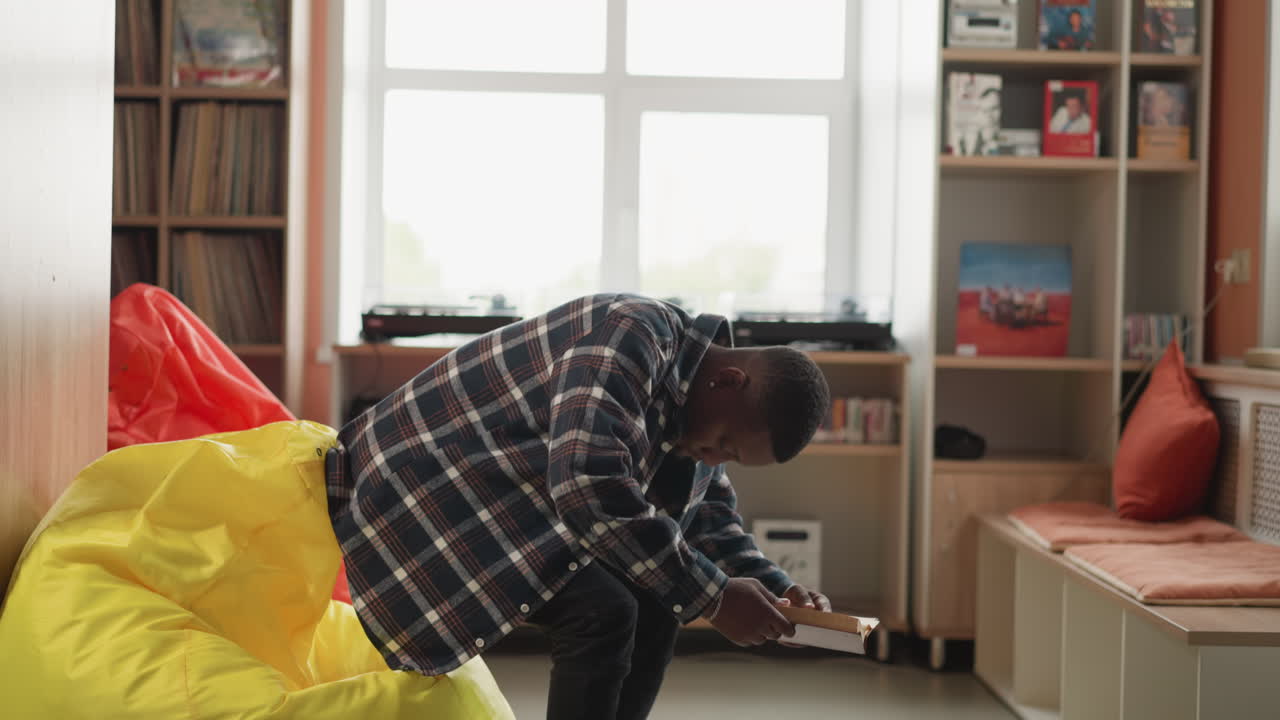 남자가 대학 도서관에서 콩 봉투에 앉아있다. 아프리카계 미국 학생은 현대 서점에서 편안하게 읽는 것을 즐긴다. 교육과 취미