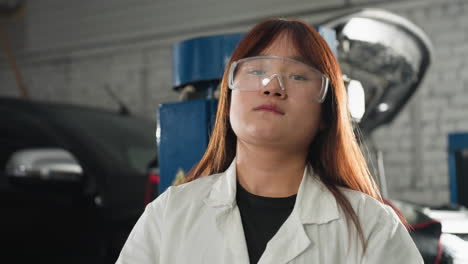 inventor in lab coat adjusts protective glasses while tilting head backward in automotive workshop, black car and machinery visible in background