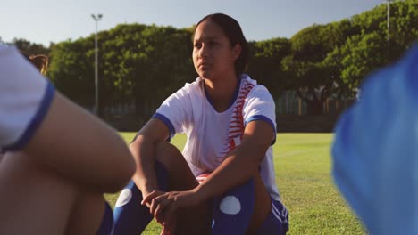 Female-soccer-player-sitting-on-the-ground-next-to-teammate-on-soccer-field.-4k