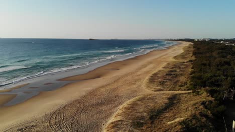 Wellen-An-Den-Weißen-Sandstränden-Australiens,-Sonnenaufgang-Mit-Dem-Surfclub-Im-Hintergrund