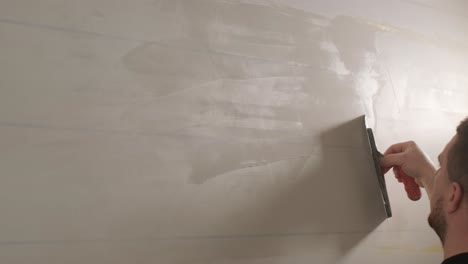 man plastering the walls with finishing putty in room with putty spatula