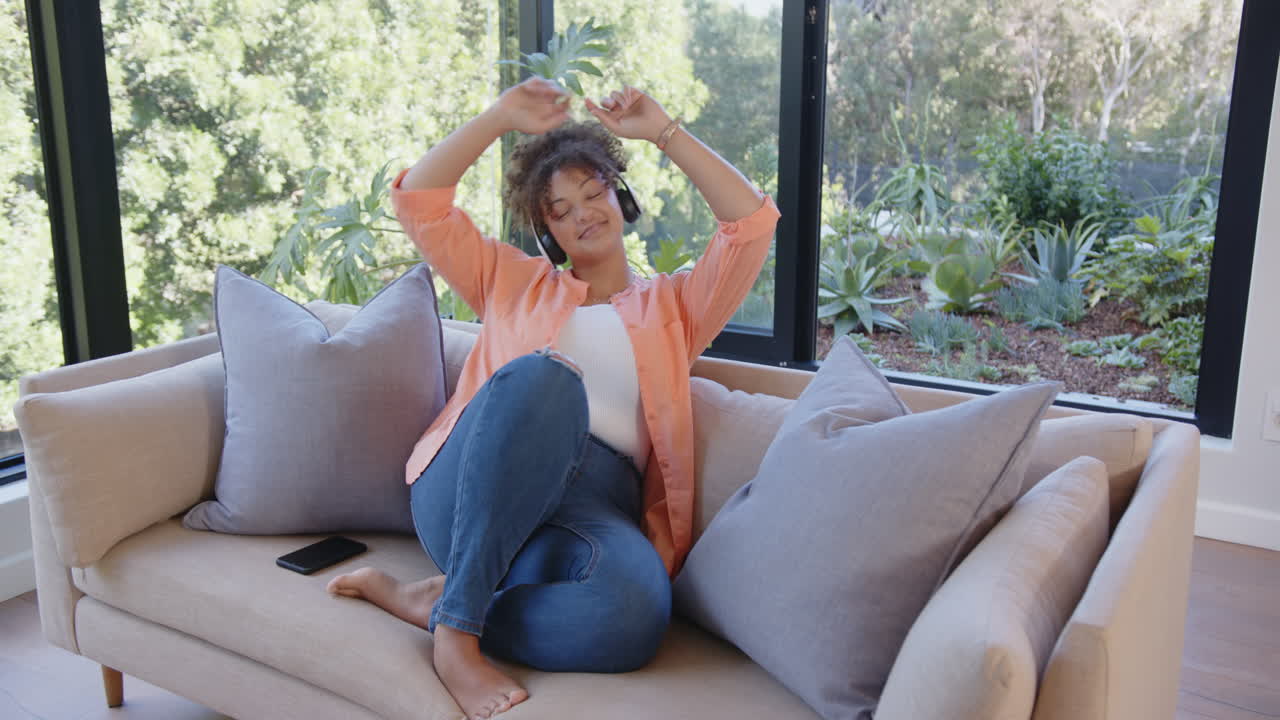 Listening to music with headphones, woman relaxing on couch with smartphone nearby