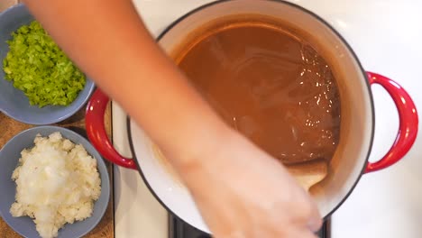 stirring the roux base for the flour to continue to brown before adding the onions and celery - overhead slow motion gumbo series