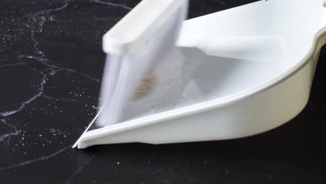 cleaning a dark marble surface with a dustpan and brush