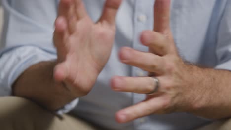 close up of man with fingers interlocked sitting on sofa talking with female counsellor about general or mental health issue