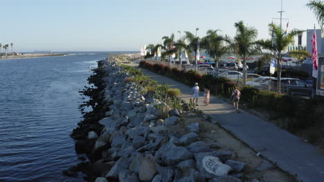 Tropical-coastline-of-Los-Angeles-with-young-person-skateboarding,-aerial-view