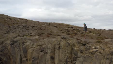 Epic-shot-of-a-young-man-standing-at-the-edge-of-a-cliff,-aerial-flying-around-him-and-revealing-the-view-at-Sao-Laurenco,-Madeira