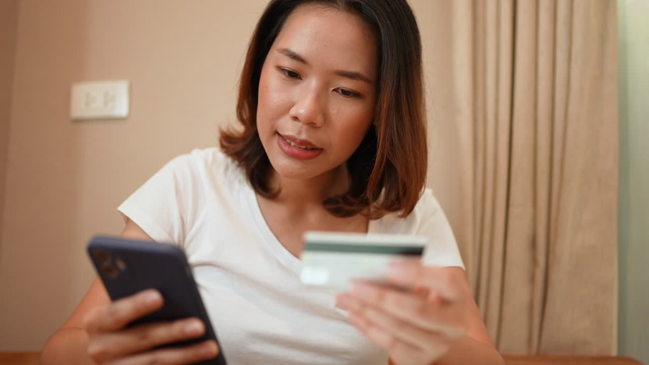 슬로모션 장면: 아시아 여성이 신용카드를 들고 스마트폰을 사용하여 온라인 쇼핑 개념을 지불하기 위해 전자 상거래 웹 사이트에서 품목을 선택합니다.