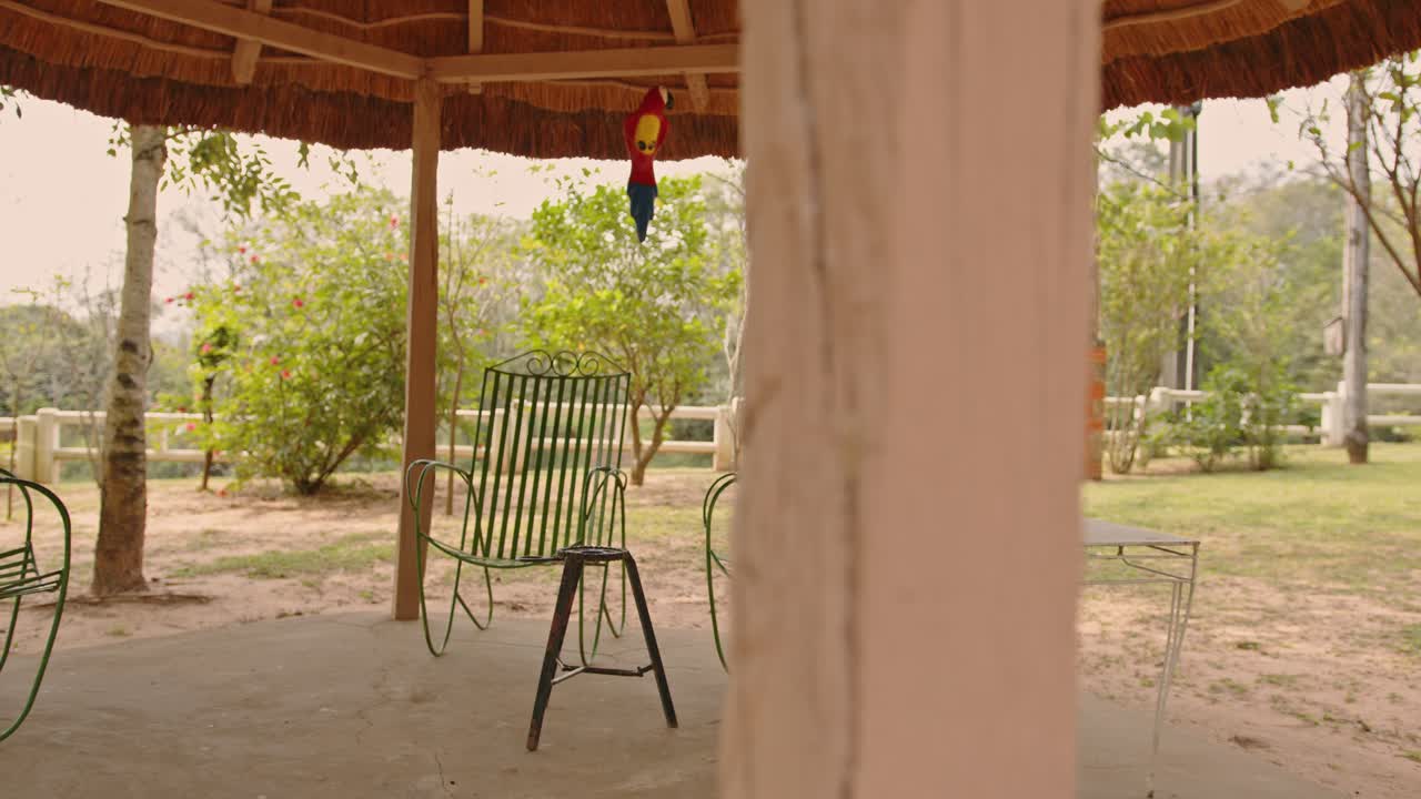 un gazebo de techo de paja en una casa de campo en paraguay, con sillas de hierro verde debajo, una mesa blanca y una pequeña mesa para terere en un hermoso