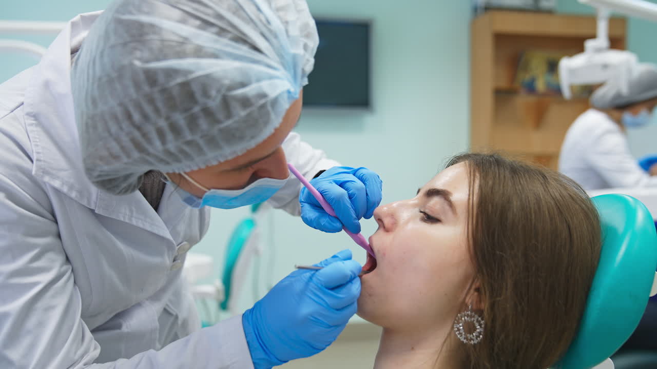 Female student bent over the patient in dentist chair. Medical student examining girl's teeth with metal instruments. Close up.