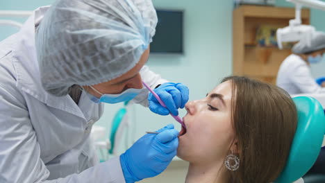 female student bent over the patient in dentist chair. medical student examining girl's teeth with metal instruments. close up.
