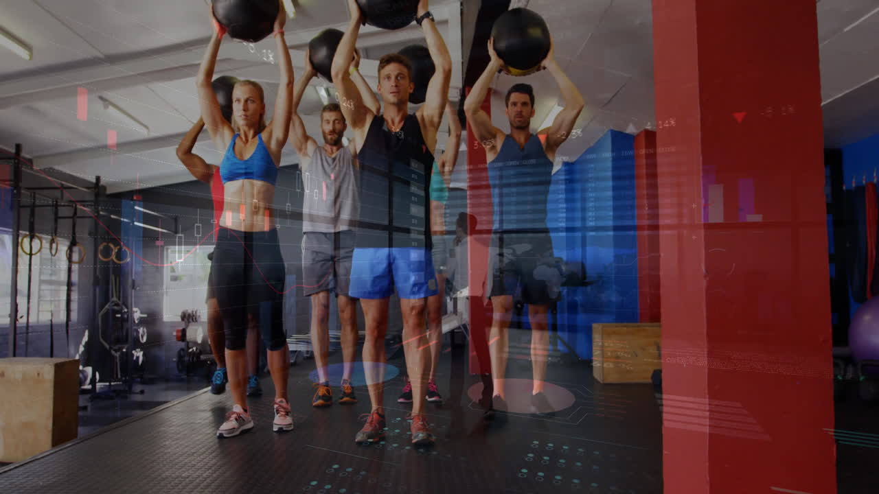 Group holding medicine balls overhead inside fitness gym, displaying floating data charts