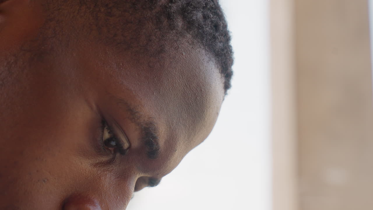 Black sport athlete closeup sweat intense, tight frame on eyes and brow, visible perspiration, window light, interior neutral background, focused stare, emotional resilience, training aftermath, raw