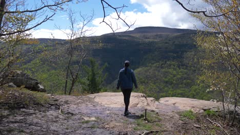 una joven excursionista camina hasta el punto de vista del sendero de senderismo en un acantilado con vistas a una excursión exitosa de días
