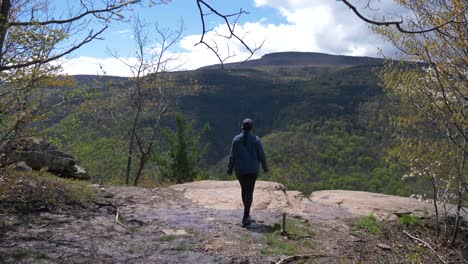 young woman hiker walks up to hiking trail viewpoint at a cliff overlook at successful days hike