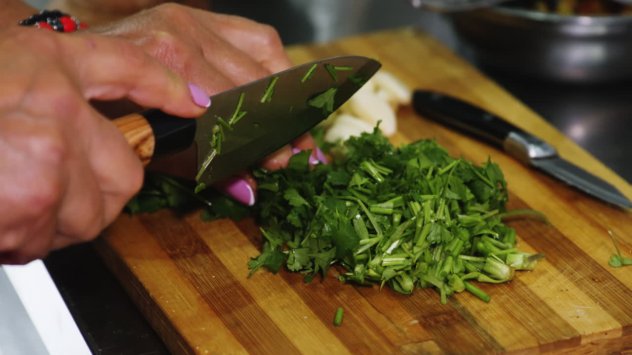 primer plano de manos de mujer con manicura cortando perejil para un plato casero