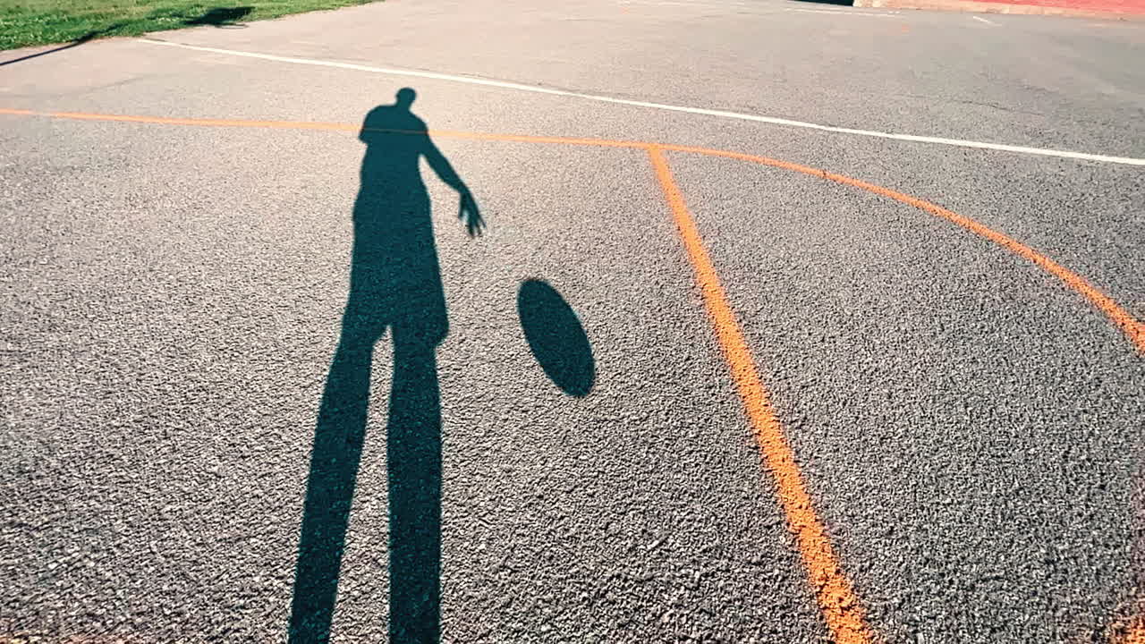 Long shadow bouncing a basketball outdoors at dusk