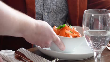 Nahaufnahme-Einer-Hand,-Die-Ein-Orangefarbenes-Nudelgericht-Auf-Einem-Esstisch-Für-Ein-Abendessen-Als-Vorspeise-Serviert