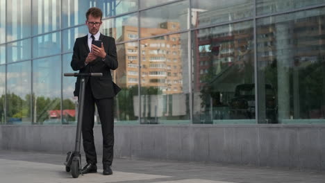 businessman using phone near electric scooter in front of a modern building
