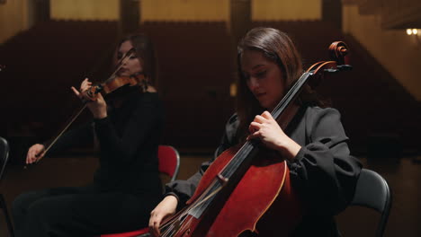 female musicians are playing cello and violins on scene of old opera house