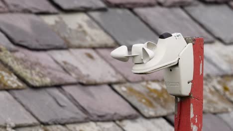 close-up of a rooftop anemometer mounted on a red pole with a tiled roof backdrop.