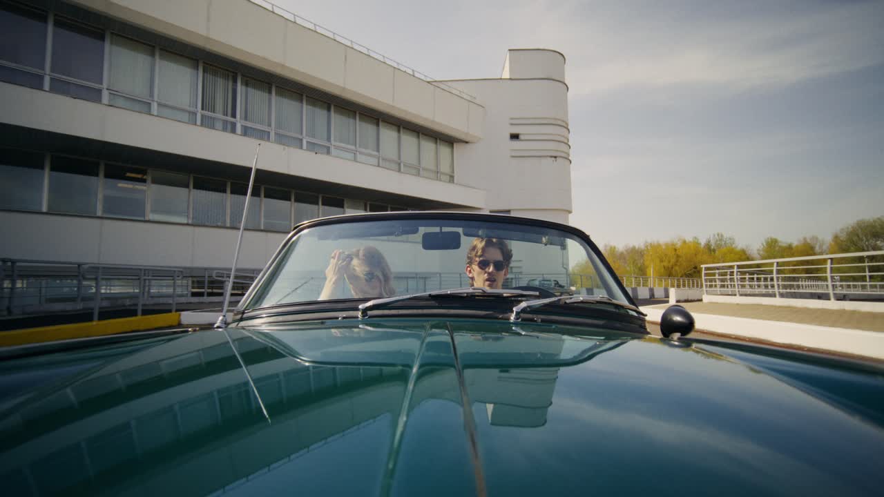 Vintage Convertible Car with People in front of Modern Architecture