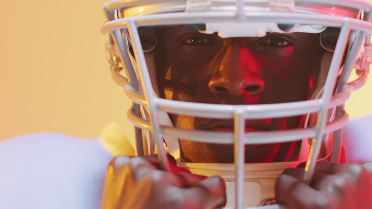 Video di giocatore di football americano afroamericano con casco su sfondo da giallo a arancione