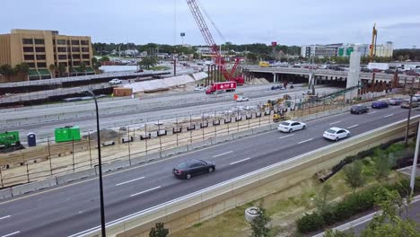 slow panning low aerial drone shot of busy highway exit showing bridge overpass intersection with vehicular traffic, road construction zone, road construction equipment, and crane