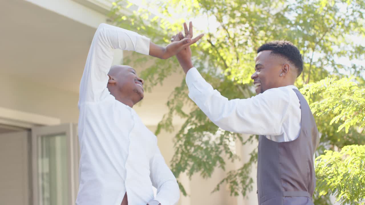 Happy african american gay male couple dancing together at wedding, slow motion
