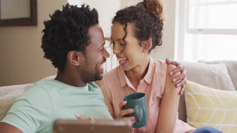 happy biracial couple sitting on sofa and having video call on smartphone