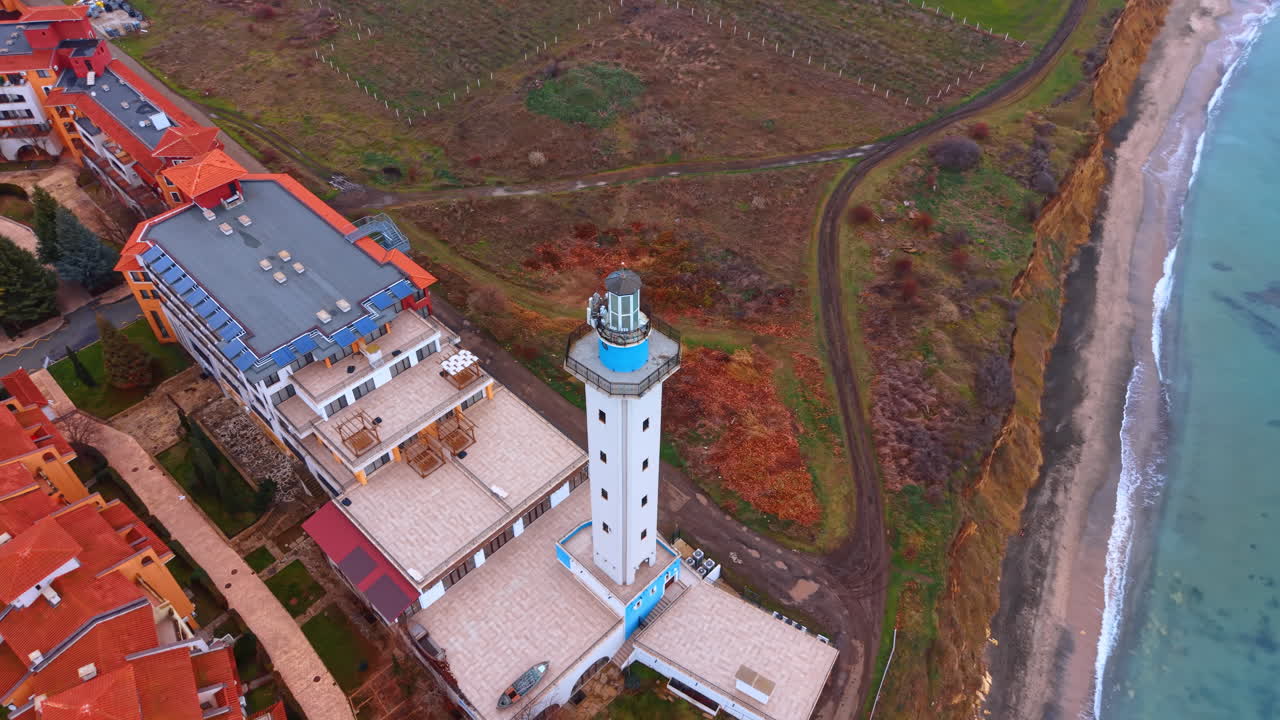 Vista dall'alto di un faro sulla costa marina. Ripresa aerea dall'alto di una torre faro, di una spiaggia e di acque turchesi in una giornata nuvolosa.