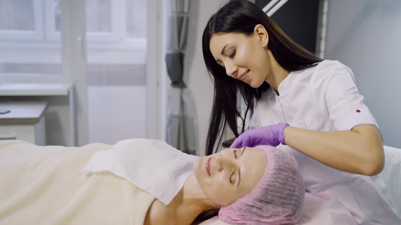 A cosmetologist makes injections for a woman in a beauty center. The client is laying on the couch during the procedure. Mesotherapy.