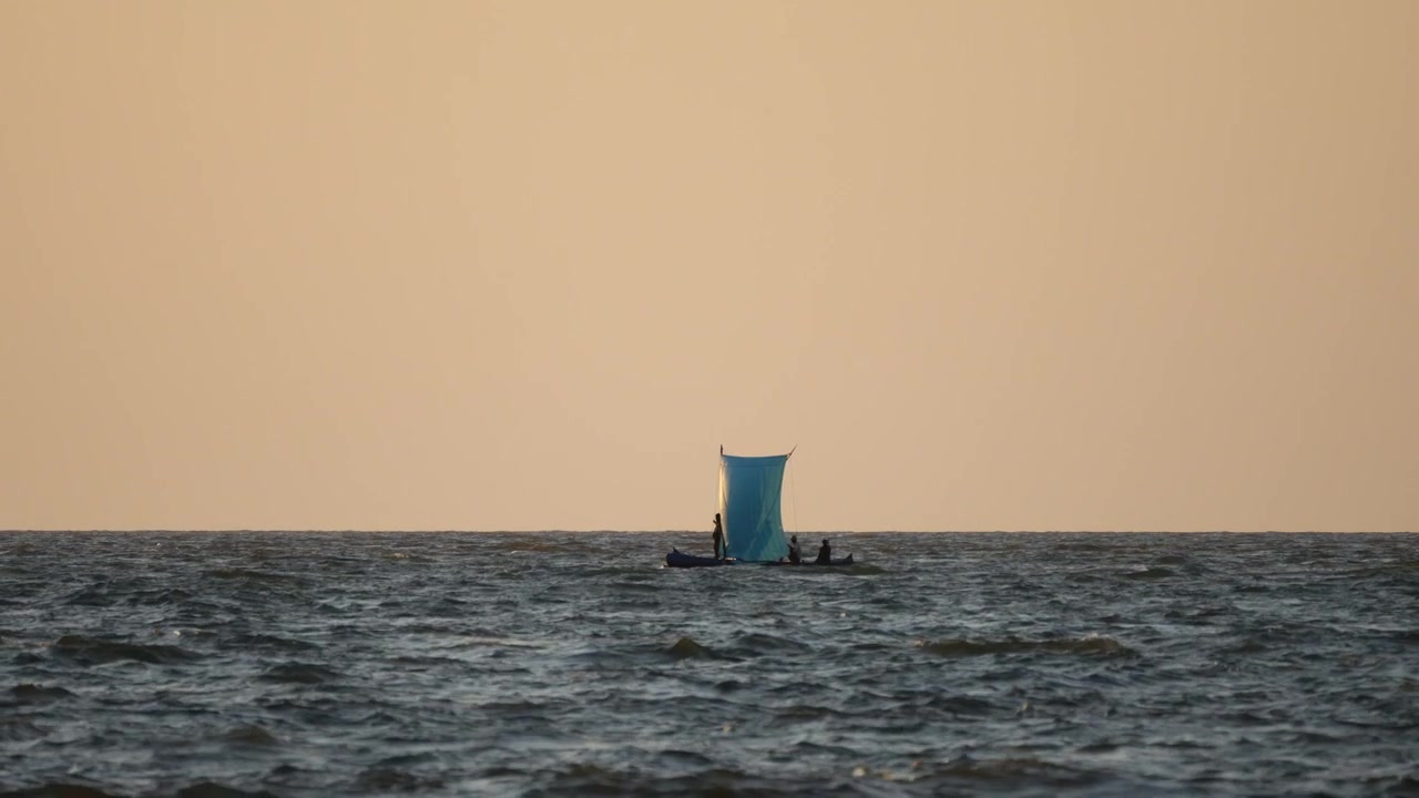 Telephoto shot of a traditional Malagasy outrigger canoe sailing on choppy ocean water during a golden sunset in Mahajanga, Madagascar.