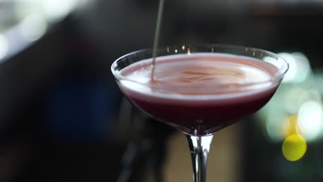 bartender mixing ingredients in fruity red cocktail martini, closeup