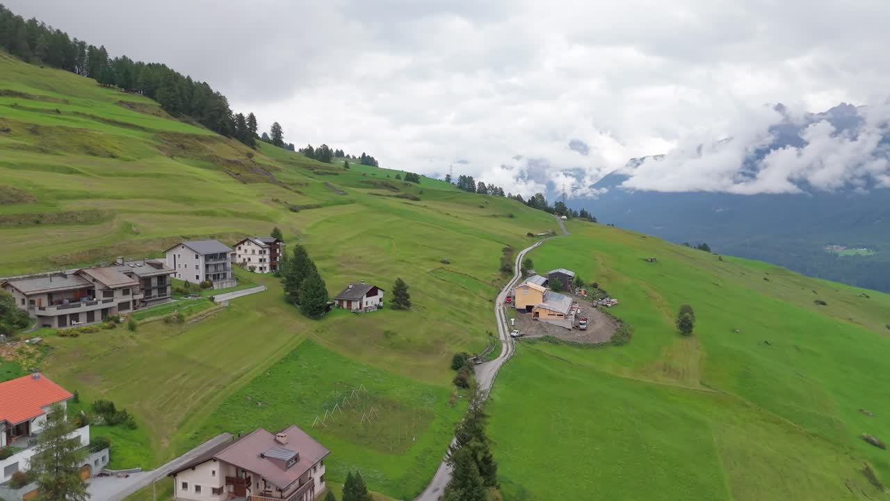 Swiss apartment huts on green alps with clouds in distance. Hovering cloudscape between mountains. Aerial forward wide shot