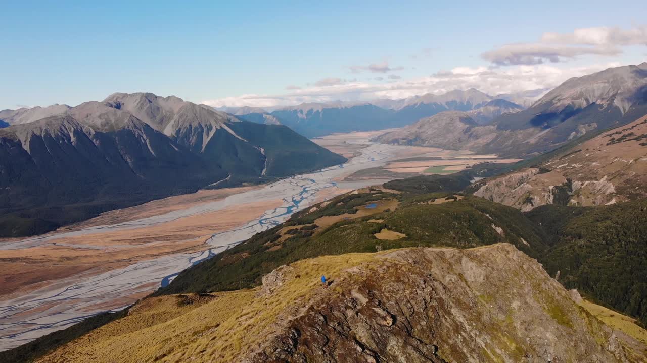 Drone Descending Towards A Hiker Standing On The Mountain Ridge Overlooking The Beautiful Bealey Spur Track In Arthur's Pass National Park, New Zealand - aerial