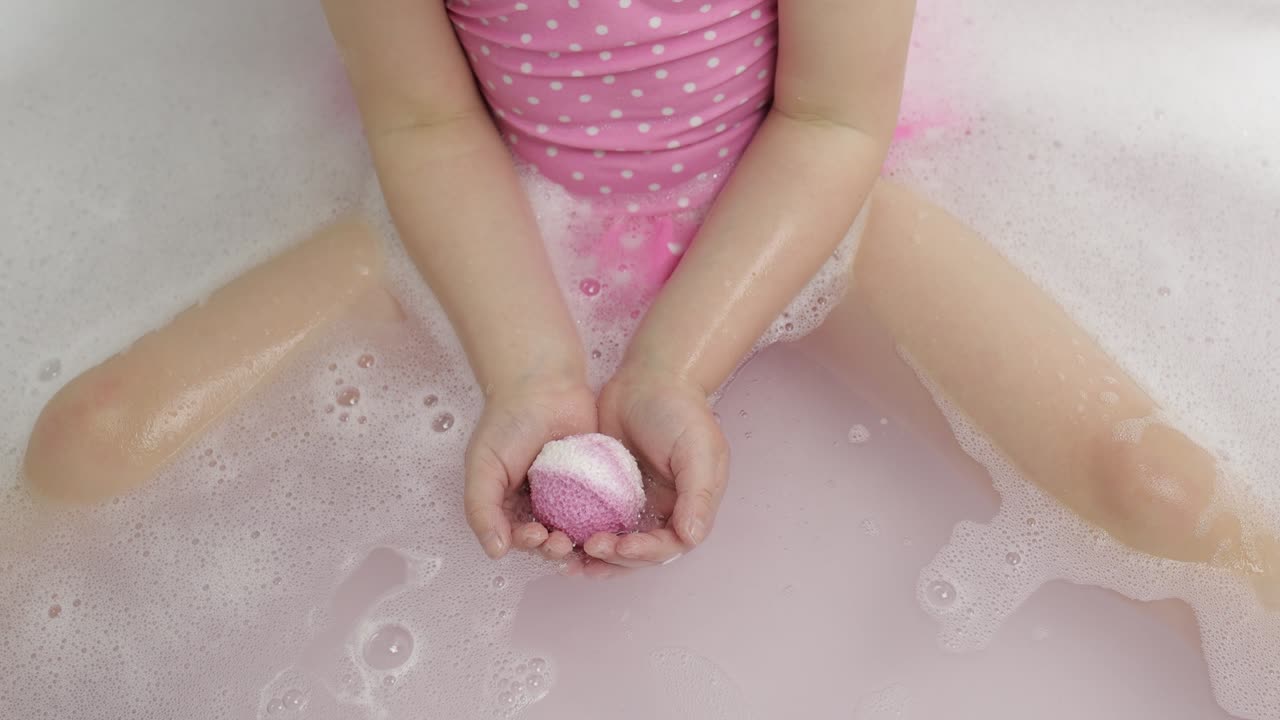 Manos de chica ponen bomba de baño en el agua. Bola de sal de baño se disuelve en el agua