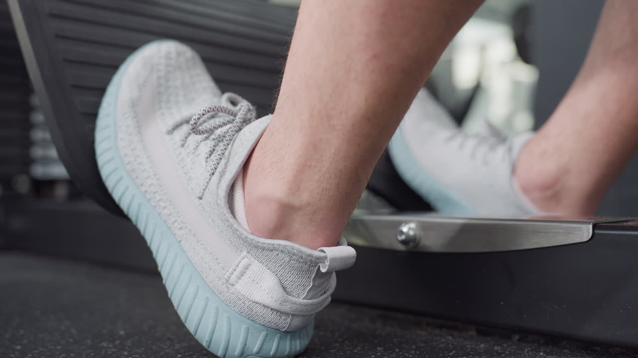 Gym trainer places foot on weight machine pedal, leg tightening with powerful contraction as he pushes resistive load for intense leg workout in gym with visible muscle engagement